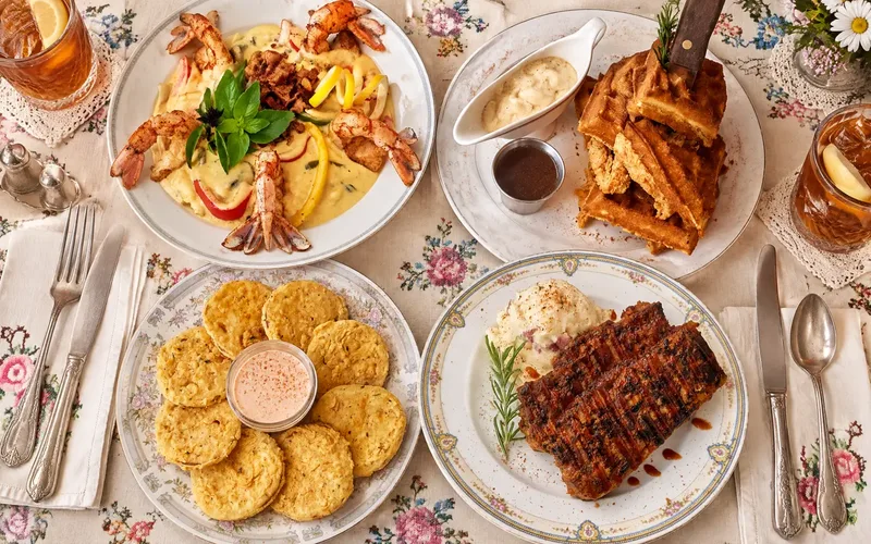Shrimp & Grits, Chicken & Waffles, Fried Green Tomato Appetizer, Southern Style Meatloaf on Mashed Potatoes on china plates, with floral tablecloths, vintage floral linens and vintage silver cutlery, iced tea in cups on doilies, silver salt